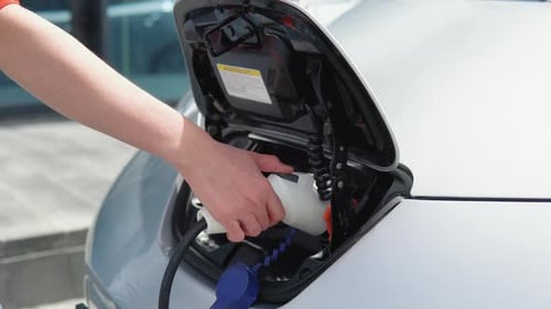 Nahaufnahme einer Mädchenhand, die das Ladegerät ihres Elektroautos herauszieht