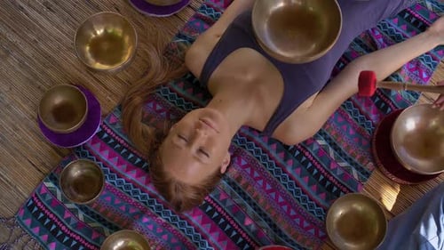 Woman Lays Surrounded by Singing Bowls for Therapy