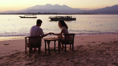 Couple silhouettes, having a romantic date on beach at sunset.