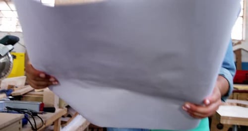 Woman Reviews Blueprints in Workshop Wearing Safety Glasses