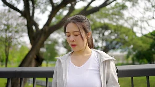 4K Asian woman drinking water from a bottle while jogging at public park in the morning.