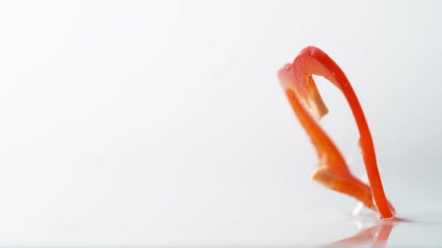 A sliced red pepper falling on water surface. Slow Motion.