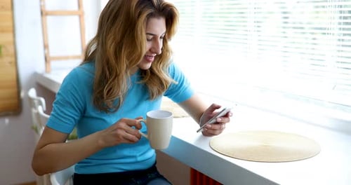 Woman Enjoys Drink and Smartphone Near Window