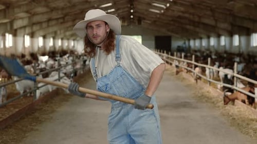 Young Farm Worker in Overalls Using Shovel for Cleaning