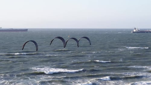 Four dark wind kites lined up together gliding in air in front of freight ships