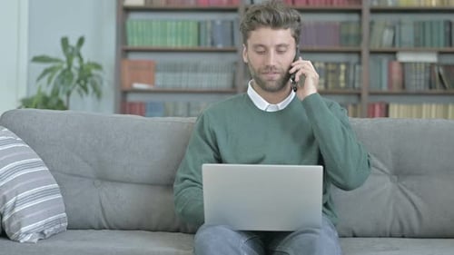 Man Talking on Phone While Using Laptop Indoors