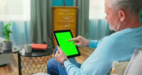 Homem mais velho em casa usa tablet com tela de maquete verde