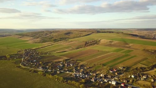 Aerial view of countryside village with small houses among green trees with farm fields