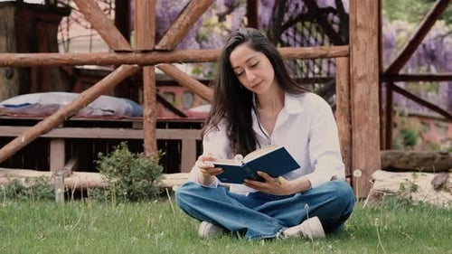 Woman Reading Book Outdoors on Grassy Lawn