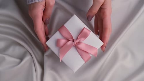 Woman Placing Gift with Pink Ribbon on Satin