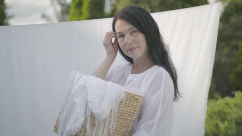 Adorable Mature Woman with Long Black Hair Holding Wicker Basket in Hands While Hanging White