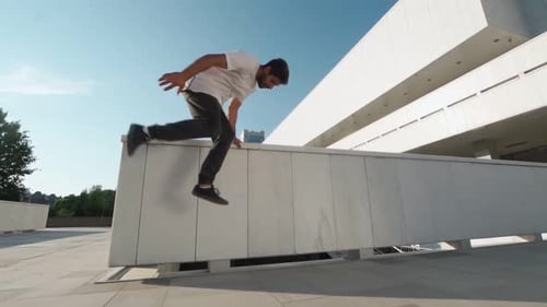 Athletic Man in White Jersey Does Back Flip Wall Against Backdrop Sunny City