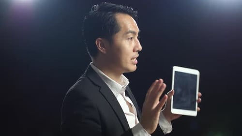 Close Up Side View Of Asian Speaker Man In Business Suit Holding Tablet While Speaking