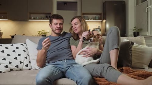 Smiling Couple Relaxing on Sofa With Small Dog