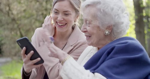 Woman and Senior Grandmother Using Smartphone Device at Park