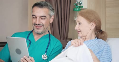Doctor Shows Tablet to Senior Patient in Hospital Bed