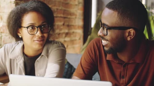 Cheerful Afro-American Coworkers Chatting and Using Laptop in Cafe