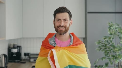 Foto de retrato de um homossexual sorridente de meia idade usando a bandeira do arco-íris sobre o ombro e olhando