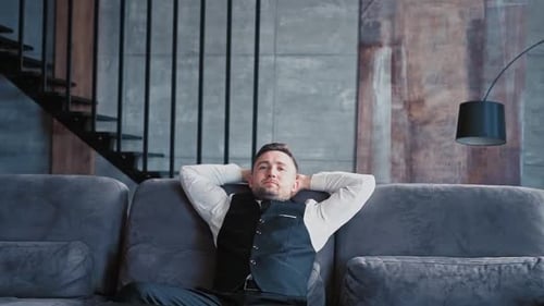 Handsome Man European Appearance Classic Clothes White Shirt Sits in Stylish Dark Office on Couch