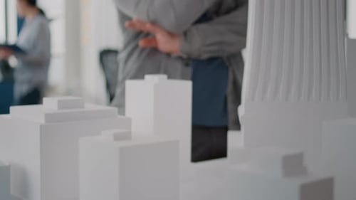 Close Up of Man Analyzing Building Model with Woman Using Blueprints Plan on Table