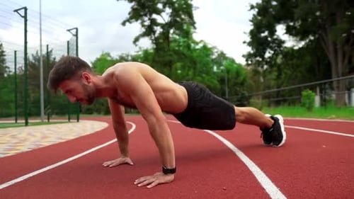 Man in Black Shorts Shirtless Doing Push Ups on Race Track Stadium Outdoors