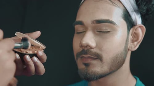 Gros plan du visage de l'homme dans un studio de cosmétiques et maquilleur mettant de la poudre sur son visage