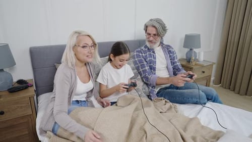 Grandparents and Granddaughter Playing Video Games on Bed