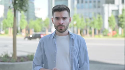Outdoor Portrait of Young Man with Finger on Lips Please Be Quiet