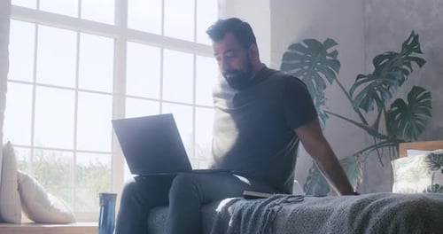 Man Works on Laptop in Sunny Bedroom