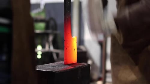 Blacksmiths forging hot metal with hammer in workshop