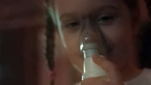 Niña inhala usando un inhalador compresor mientras está sentada en un sofá