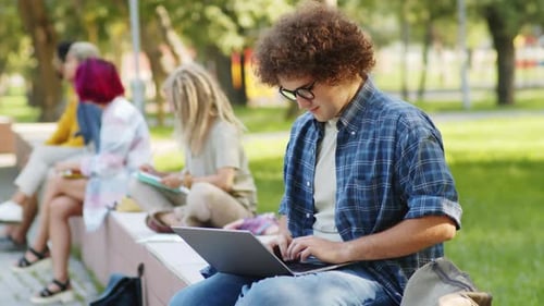 Male Student Using Laptop and Posing for Camera in Park