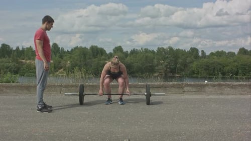 Woman Weightlifting with Man Watching Outdoors