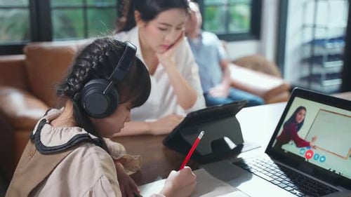 Homeschool Asian young girl learn online class from school teacher by digital remote with family.