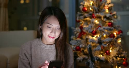 Woman Using Phone Near Christmas Tree at Night