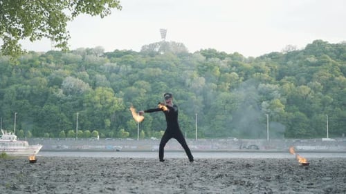 Skilled Fire Performer Twirling Burning Torches on Beach