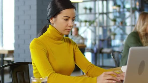 Woman Typing on Laptop in a Bright Cafe