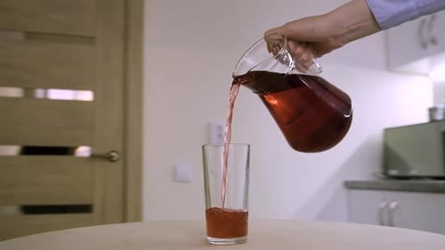 Une femme verse une compote de jus de fruits rouges dans un verre