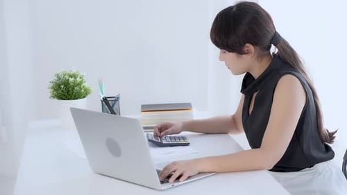 Businesswoman working calculate expenses and typing laptop computer on desk with saving finance.