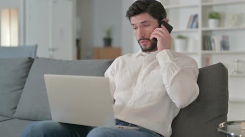 Man Working On Laptop While Talking On Phone