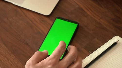Hand Swiping Smartphone with Green Screen on Desk
