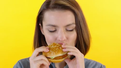 Woman Enjoys Chicken Burger on Yellow Background