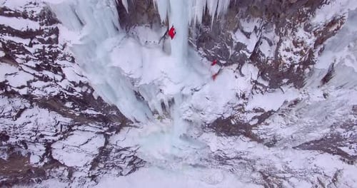 Drohnenaufnahme eines Mannes, der auf einem gefrorenen Wasserfall in den Bergen eisklettert.