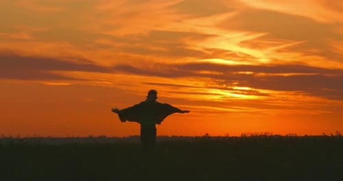 A Boy-superhero in a Green Cloak Is Running Across the Field. Face the Camera. Sunset.