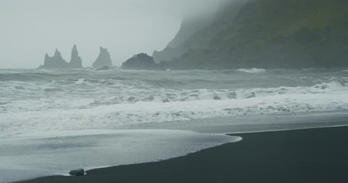 The Black Sand Beach of Reynisfjara with Waves Hitting the Shore on Foggy Rainy Stormy Day