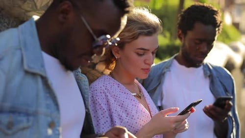 Young Adults Using Smartphones Together Outdoors in City