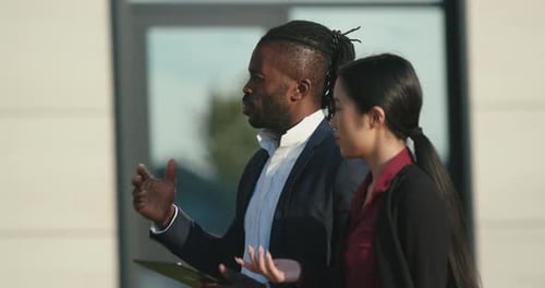 Businessman and Asian Lady with Tablet Walk Past Building