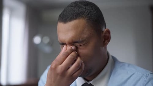 Closeup Portrait of Tired African American Young Man Rubbing Eyes Working in Home Office on Covid19