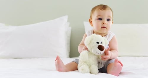 Cute baby girl playing with soft toy on bed