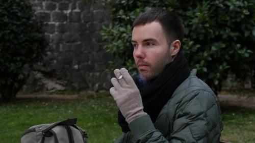 Jeune homme endormi fumant une cigarette assis sur un banc en hiver.